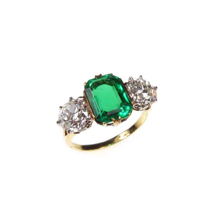 Three stone emerald and diamond ring, the central emerald-cut Colombian emerald claw set